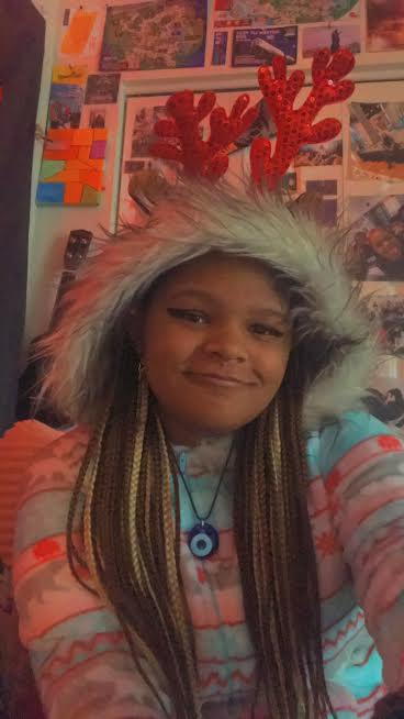 The snuggle proves real for Staff Writer Rayne Branch who sports a comfortable winter hoodie with red glitter antlers in front of her room’s photo wall with memories to last a lifetime. 