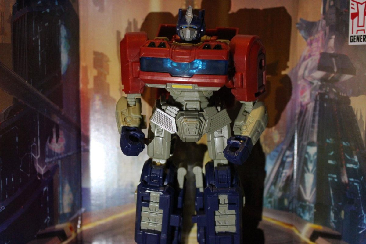 Transformers One: Studio Series Optimus Prime standing before a backdrop of Cybertron.